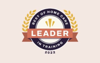 A circular emblem features "Leader in Training" in the center, surrounded by "Best of Home Care" at the top and "2022" at the bottom. The design includes a ribbon and laurel branches, emphasizing achievement. The color scheme includes orange, navy blue, and gold.
