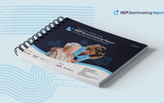 A spiral-bound book titled "12th Annual Edition of the 2023 Activated Insights Benchmarking Report for Home Care Agencies" lies on a surface. The cover displays an image of two people, one elderly, one younger, with icons of charts and communication symbols. The year "2023" is in the top corner.