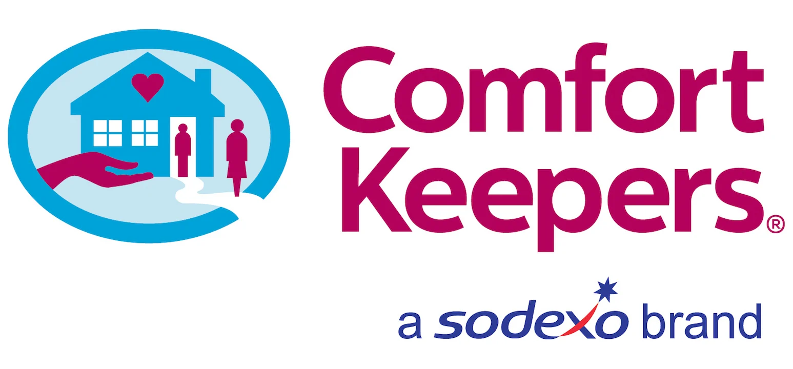 Logo featuring a blue house with two people and a heart inside, held by a hand, next to the words "Comfort Keepers" in pink and "a Sodexo brand" in blue with an orange star.